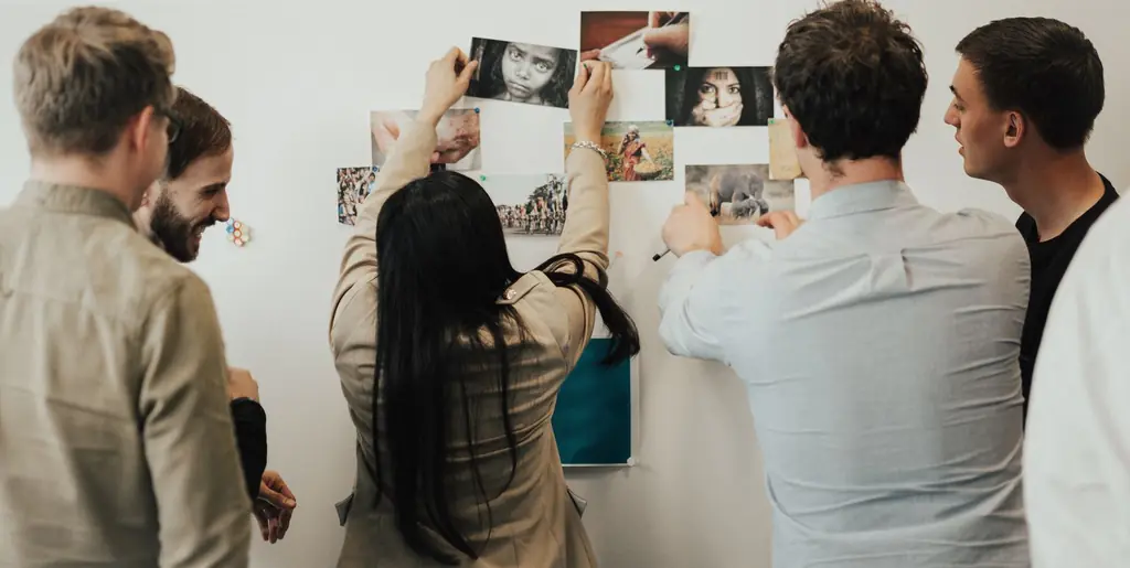 Workshop participants pin photos and notes to a wall as they map ideas together